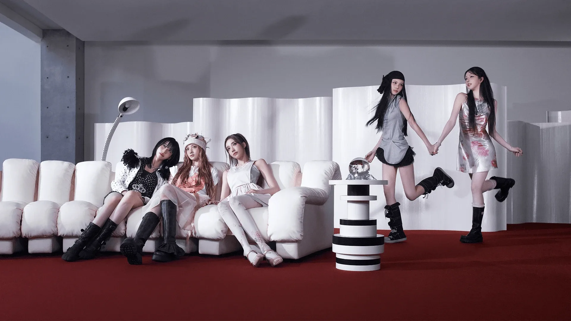 The five members of A2O MAY in a white room with a red carpet, three seated on a white sofa and two holding hands mid-step