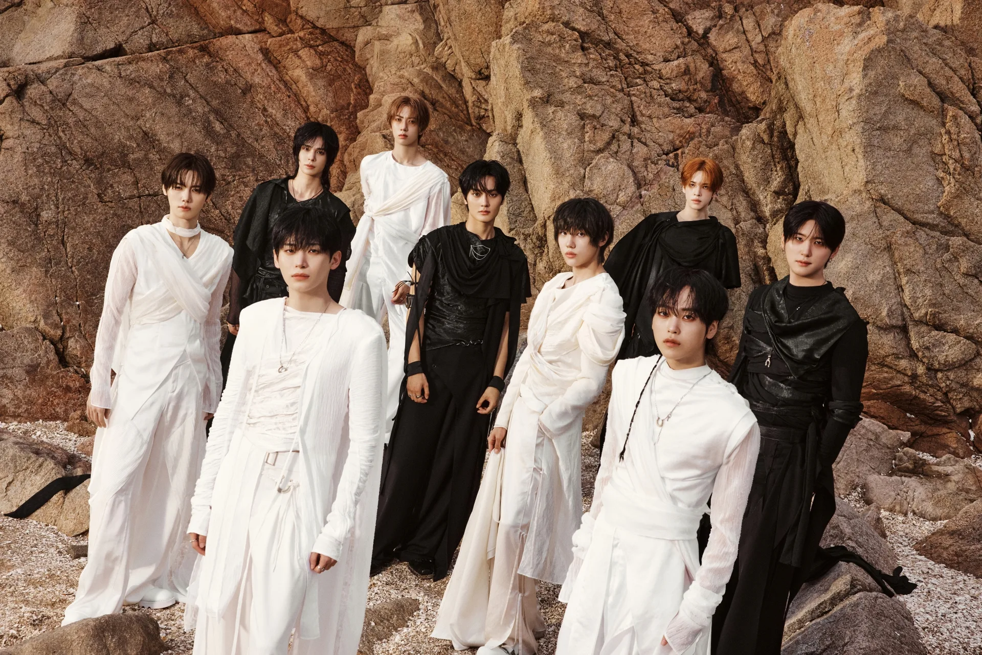 The nine members of CRAVITY in white and black outfits against a rock face, in the official sonorous-era group photo