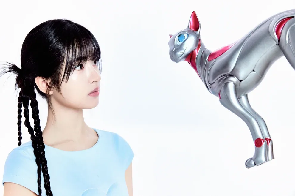 Rada of A2O LITE with braided pigtails looking away from a silver robotic cat, in her official NEON artwork